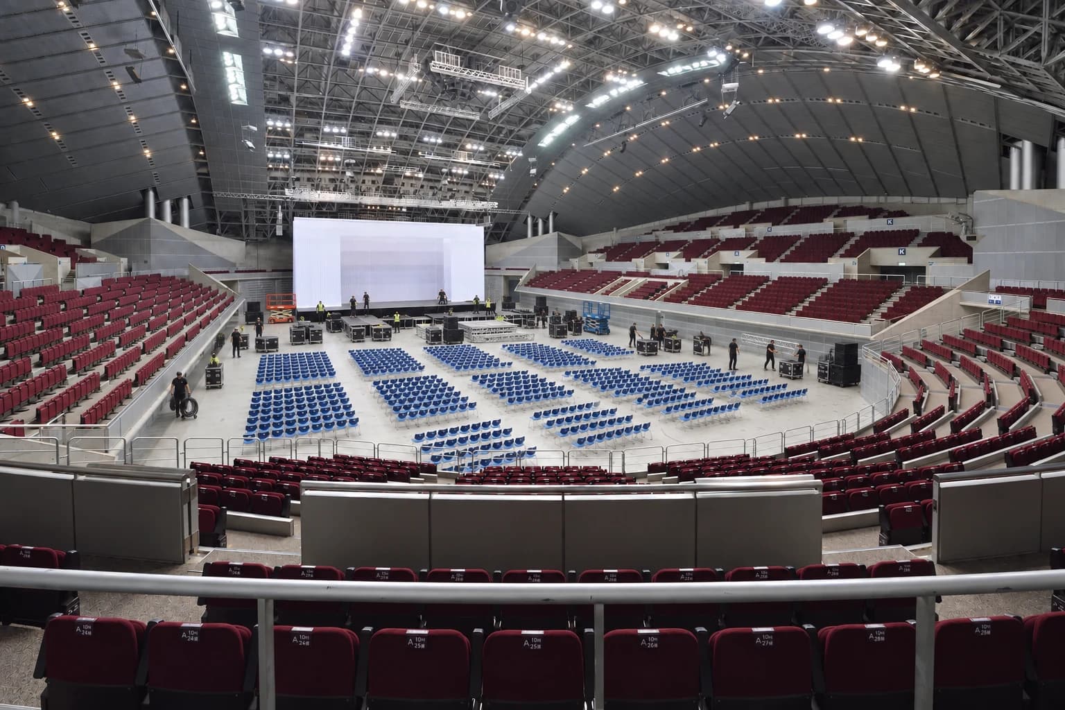 Arena floor during load-in, crew and road cases around a screen going up with the first rows of floor seating set out