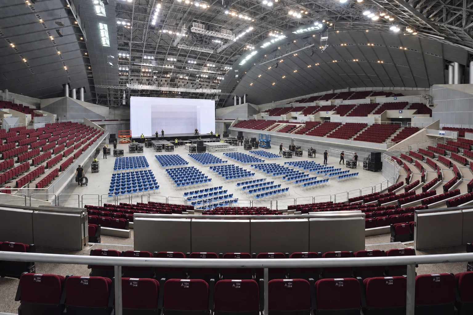 Arena floor during load-in, crew and road cases around a screen going up with the first rows of floor seating set out