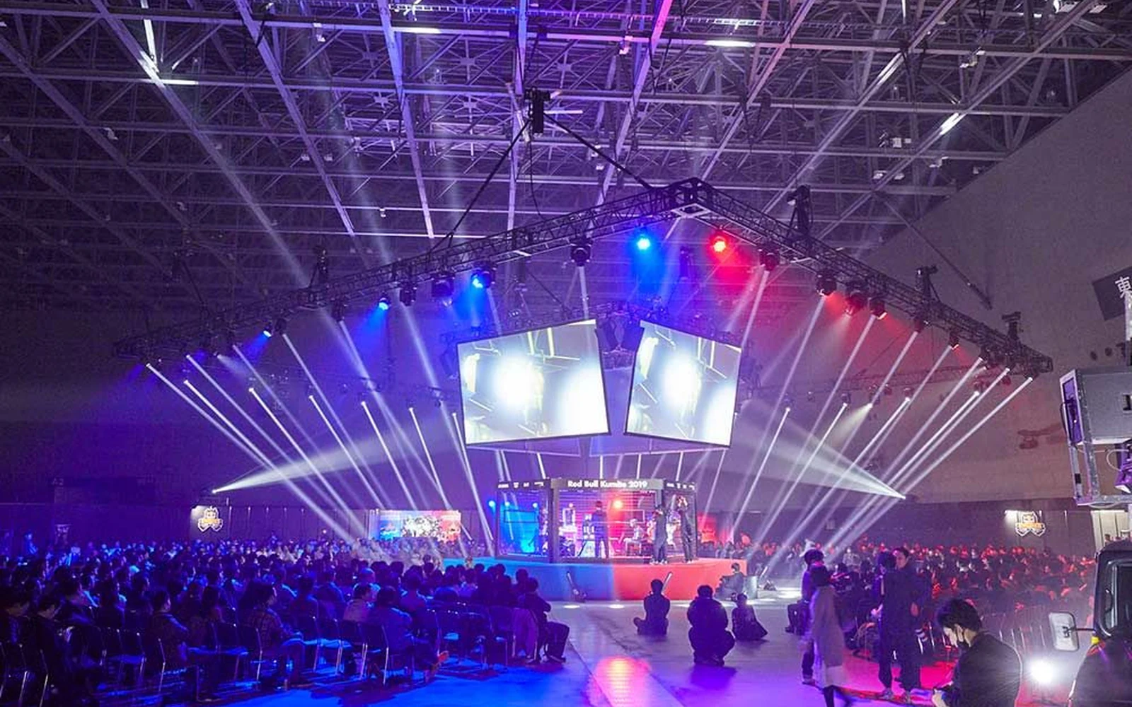 Competition stage under a temporary lighting rig at Red Bull Kumite, twin screens above the players and the floor audience seated in front
