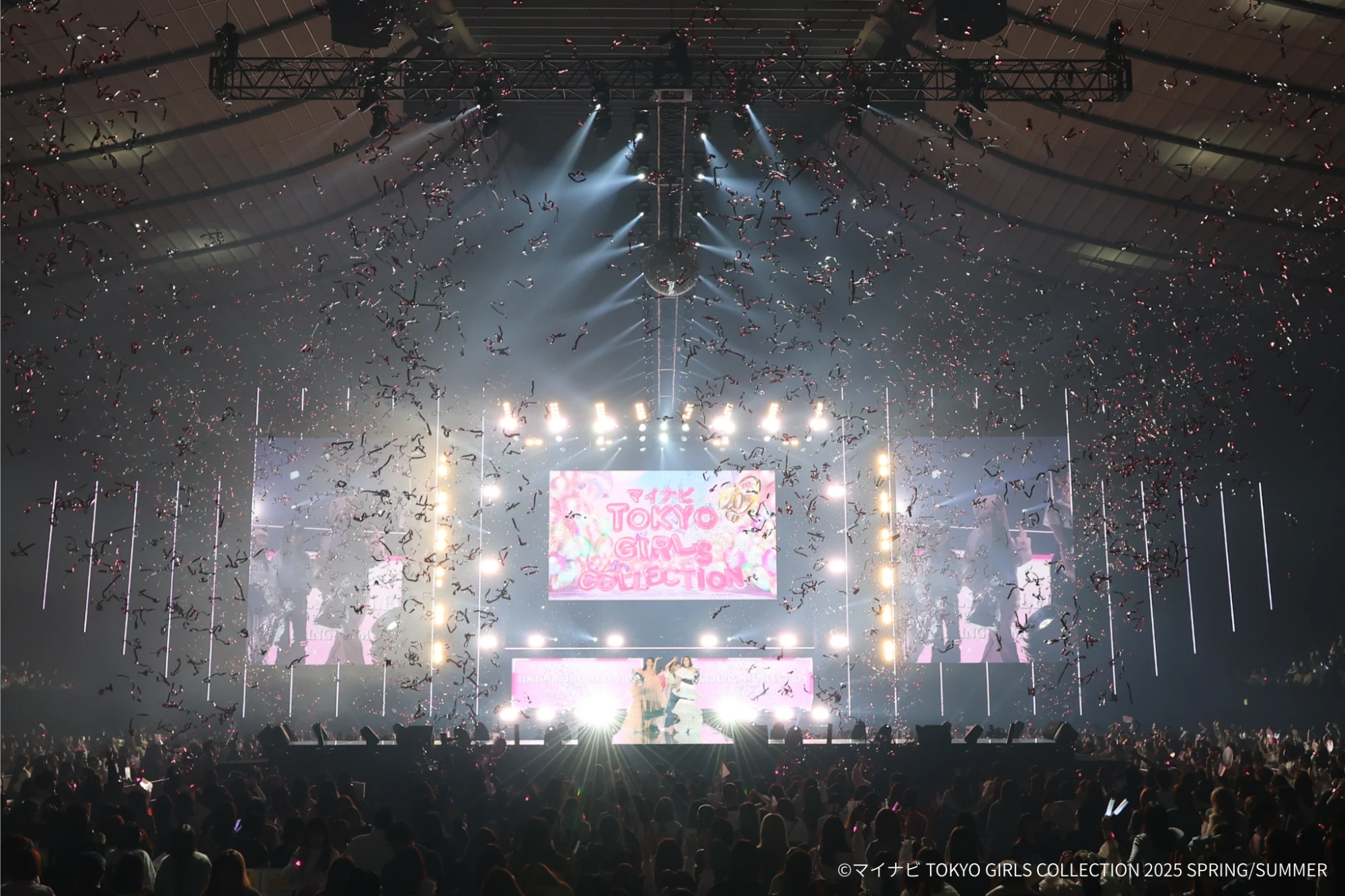 Tokyo Girls Collection finale under falling confetti, centre screen and flanking screens carrying the show artwork above the stage